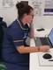 Nurse wearing a navy blue tunic, sitting at her desk looking at her laptop