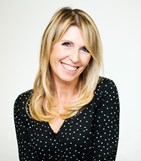 Picture of Alex Green smiling at the camera. Wearing a black top with white dots.