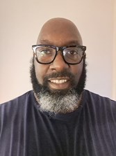 Photo of Tola, cooproduction lead. Man with a beard, wearing glasses and a black top with white stripes