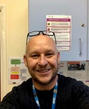 Photo of Mark smiling at the camera. He is wearing a black top.