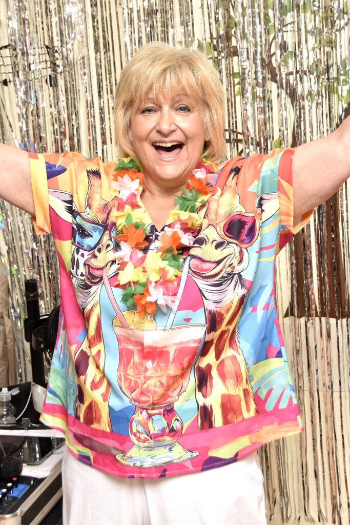 Lady wearing a bright top smiling at the camera with her hands in the air.