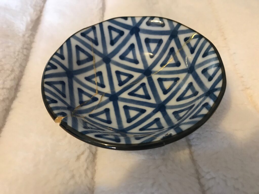 A small blue and white patterned Kintsugi bowl with gold inlay, highlighting the cracks where it was once broken but had been mended.