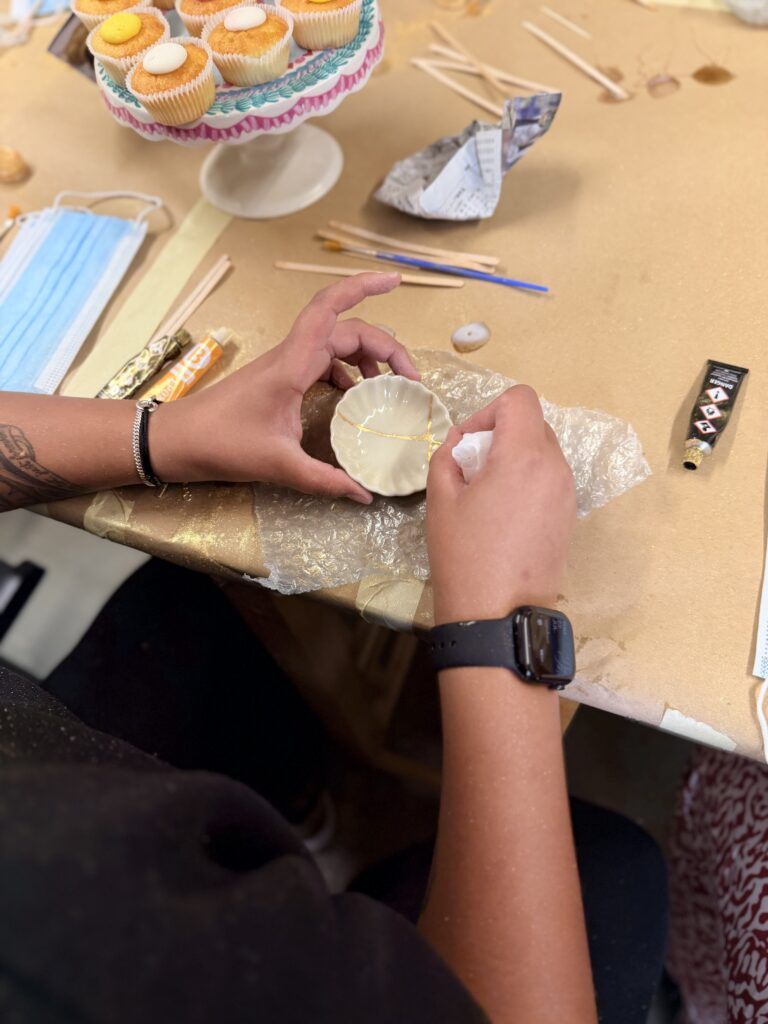 A small white Kintsugi bowl is held in two hands while the person holding it wipes excess gold from the cracks.