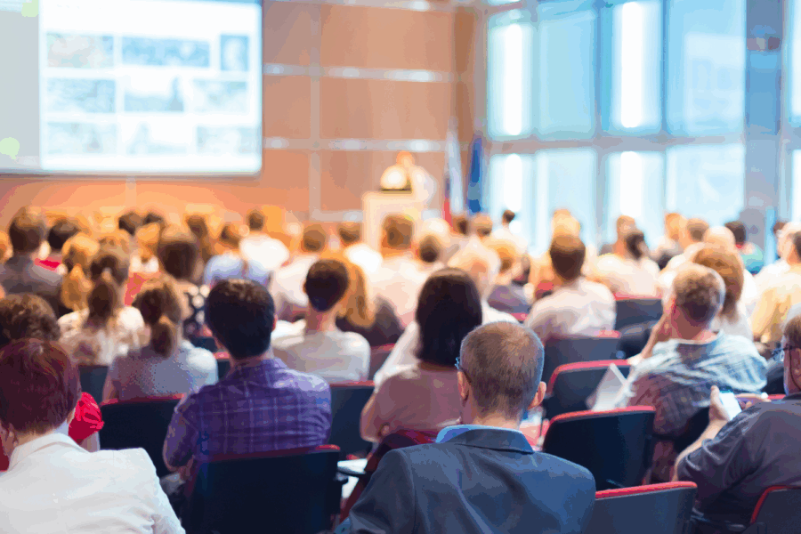room filled with people attending a meeting looking and listening to a presentation.