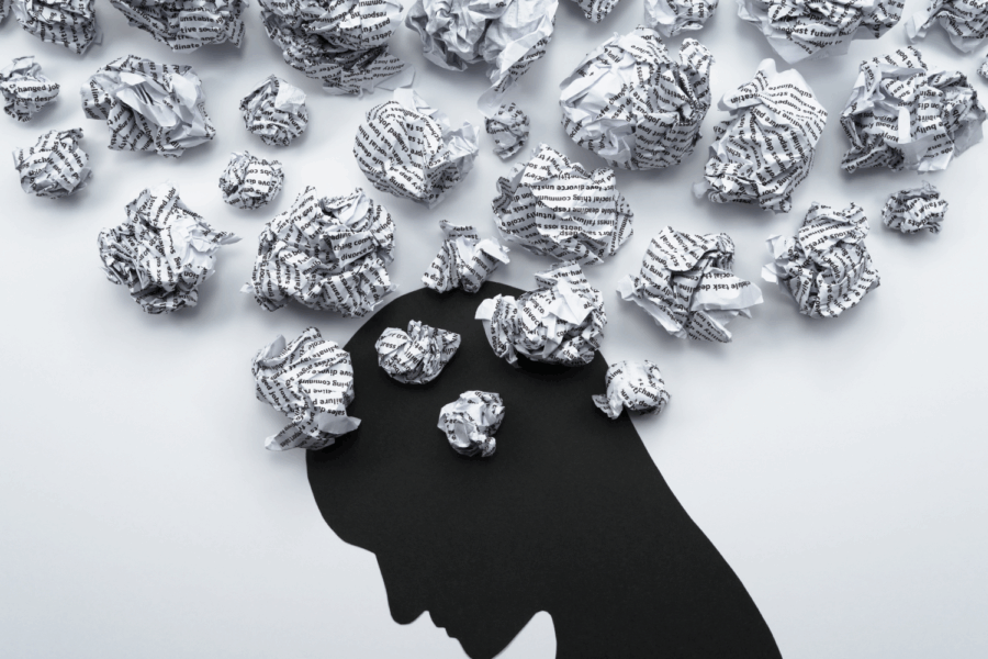 Black silhouette of a head with scrunched of bits of paper coming out of its head. This is to represent all the different scattered thoughts.