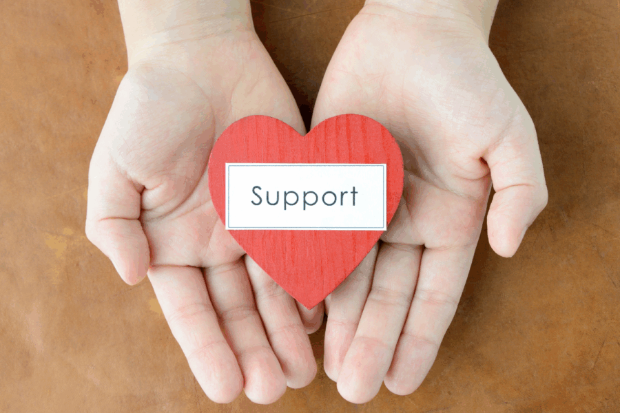 Picture pf hands holding a cut out shaped like a heart with the words 'support' on it.