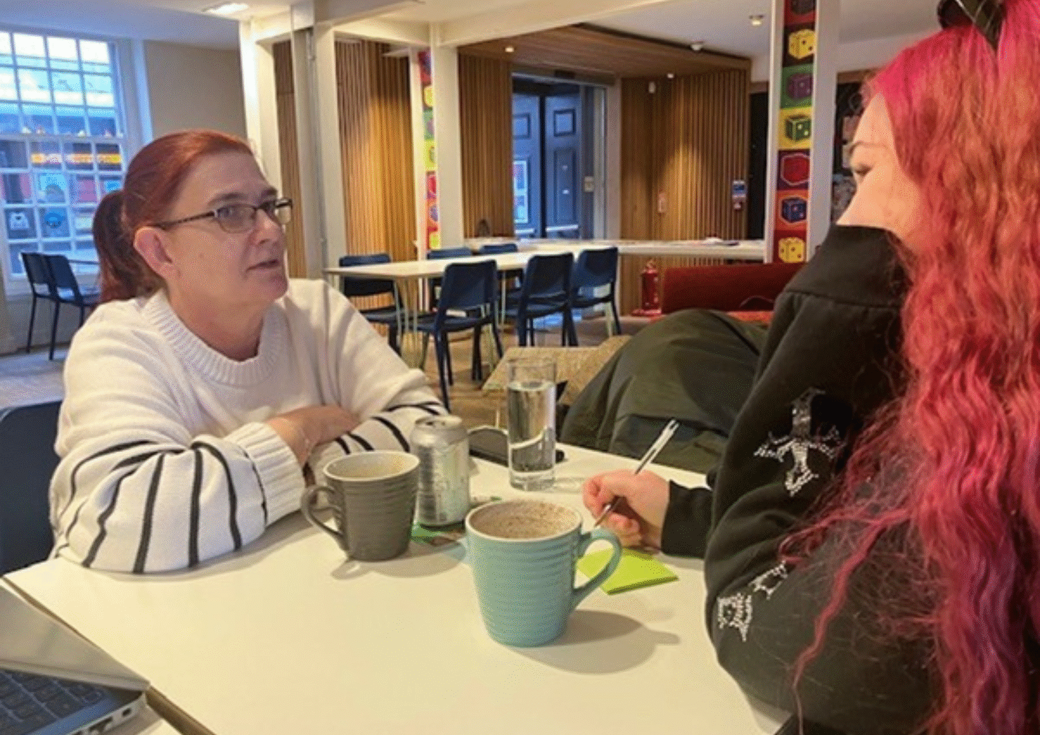 Two people in a coffee shop, talking over a drink.
