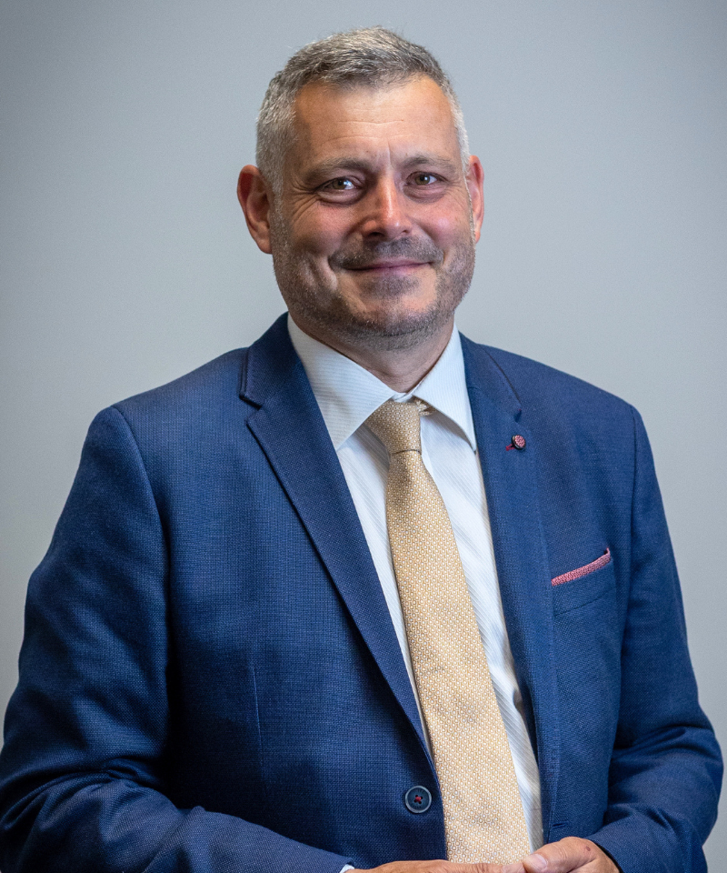 Caucasian man wearing a navy blue suit and salmon coloured tie - smiling at the camera