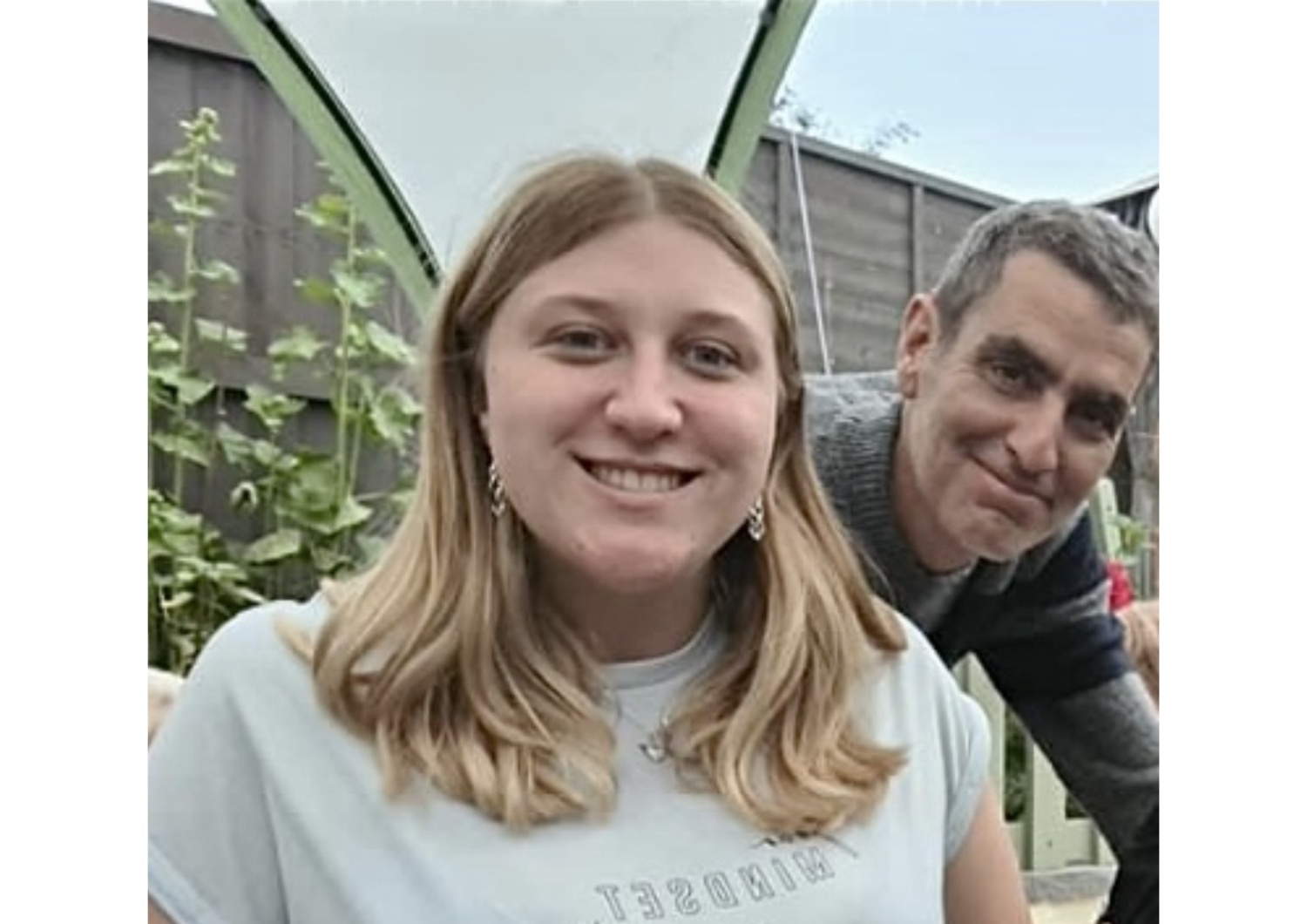 Sophie Phillips smiling outdoors next to her father, who leans in with a gentle smile.