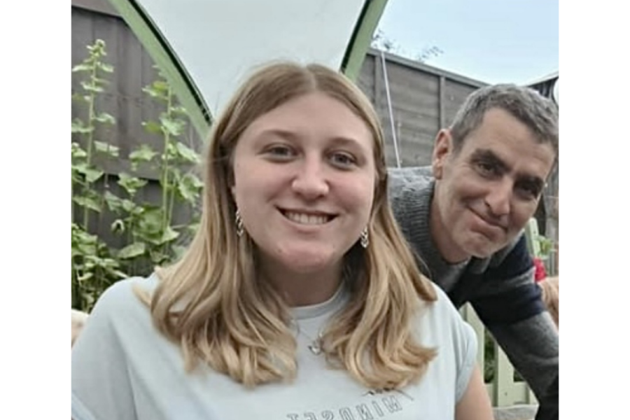 Sophie Phillips smiling outdoors next to her father, who leans in with a gentle smile.