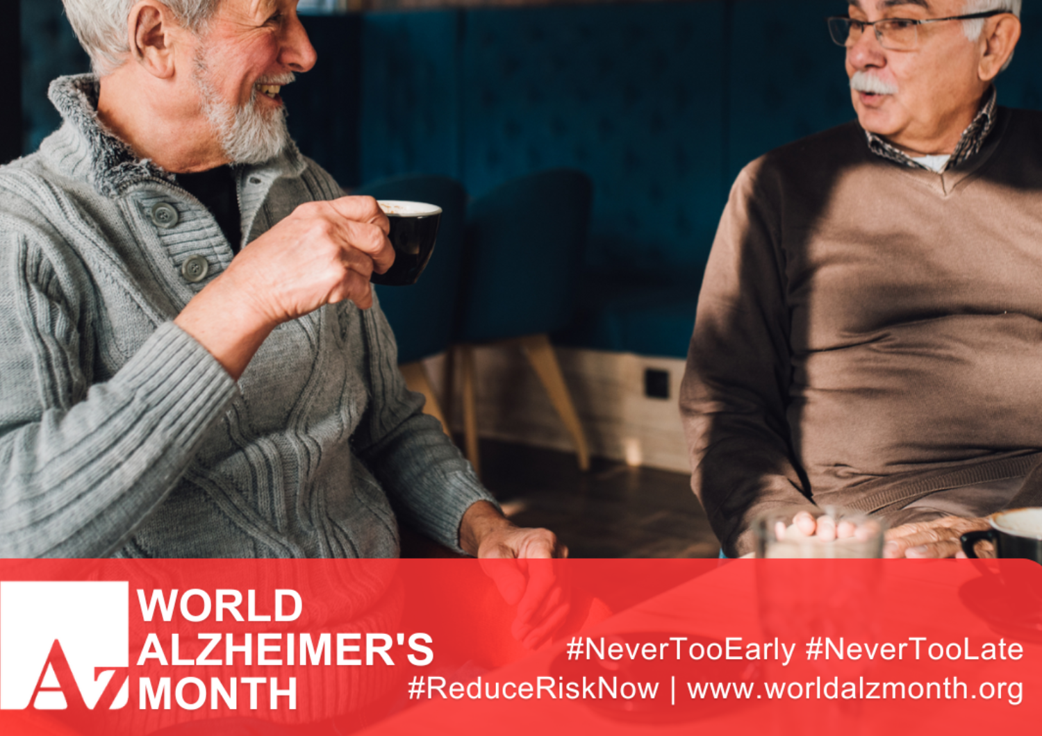 Two older men sitting together and sharing a conversation over coffee. The image features a red banner along the bottom promoting World Alzheimer's Month, along with the website address www.worldalzmonth.org and the campaign hashtags #NeverTooEarly, #NeverTooLate, and #ReduceRiskNow.