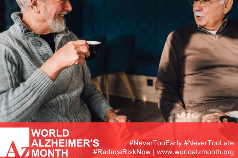 Two older men sitting together and sharing a conversation over coffee. The image features a red banner along the bottom promoting World Alzheimer's Month, along with the website address www.worldalzmonth.org and the campaign hashtags #NeverTooEarly, #NeverTooLate, and #ReduceRiskNow.