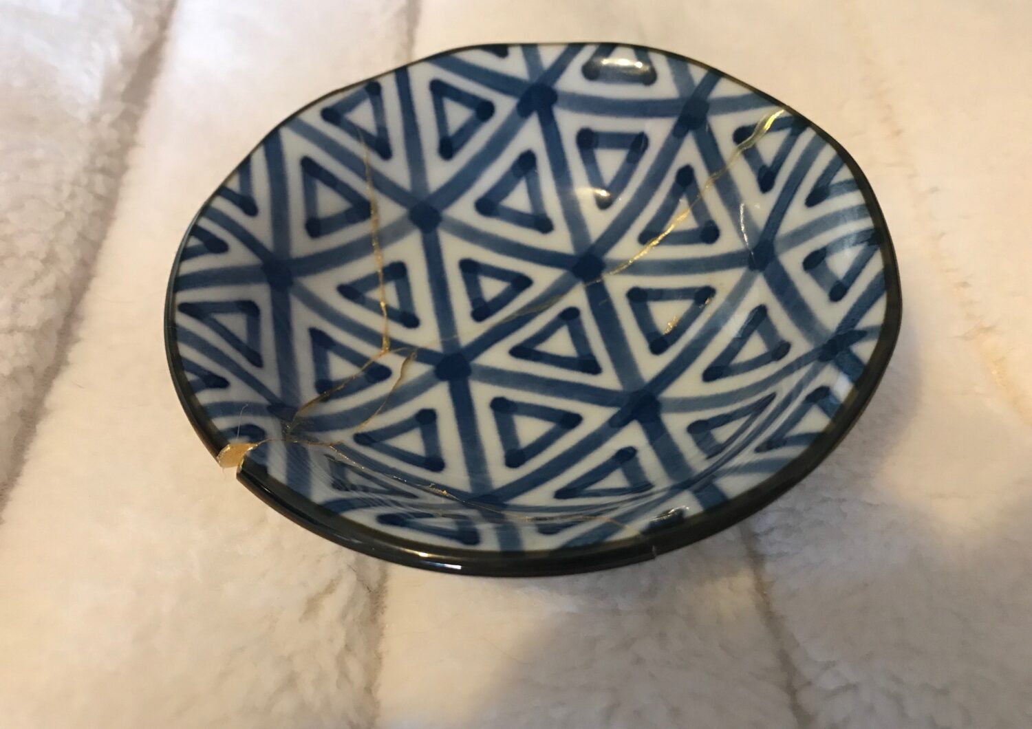Image of a small black and white patterned Kintsugi bowl. It has been broken then put back together with the cracks highlighed in gold.