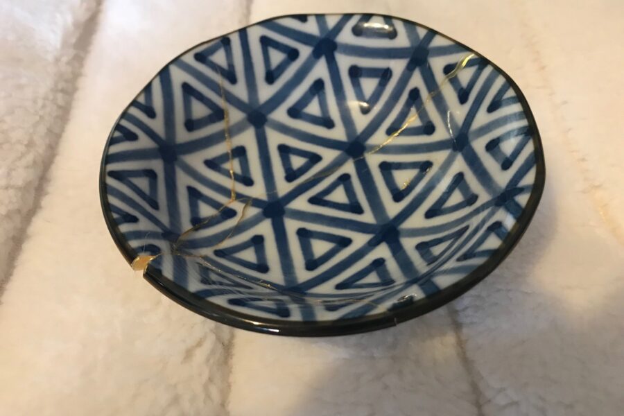 Image of a small black and white patterned Kintsugi bowl. It has been broken then put back together with the cracks highlighed in gold.