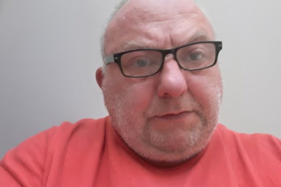 Simon Cross, wearing an orange top, wearing glasses.