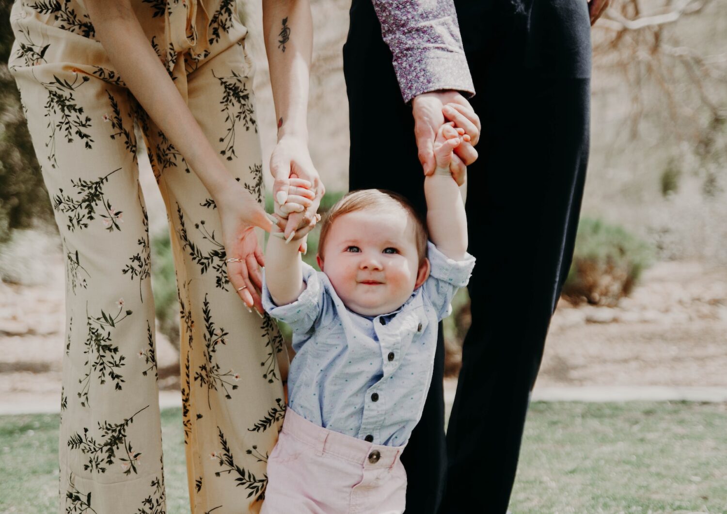 Baby taking first steps holding hands with adults.