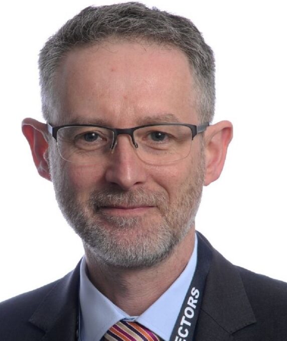 Photo of new non executive director Richard Spencer. Richard has a short beard, wears glasses and is wearing a suit, light blue shirt and a striped tie.